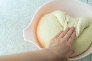 folding bread dough on itself in bowl