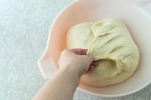 folding bread dough on itself in bowl