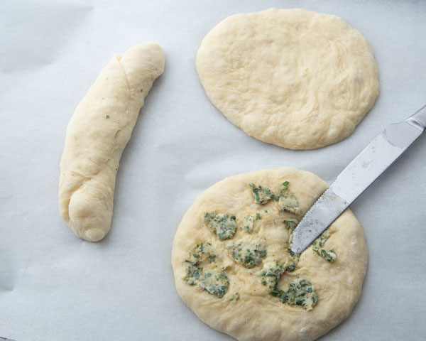 spreading garlic butter on flattened dough