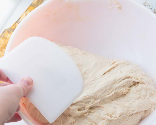 stretching and folding dough on itself with bowl scraper