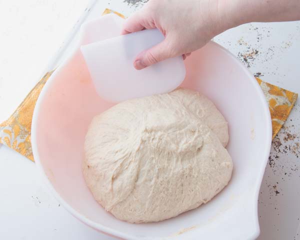 stretching and folding dough on itself with bowl scraper