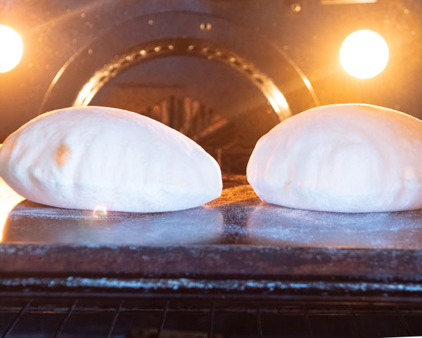 inflated pita bread baking in oven on inverted baking sheet