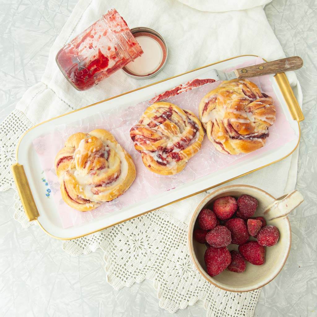 strawberry jam rolls on plate with strawberries, strawberry jam and offset spatula