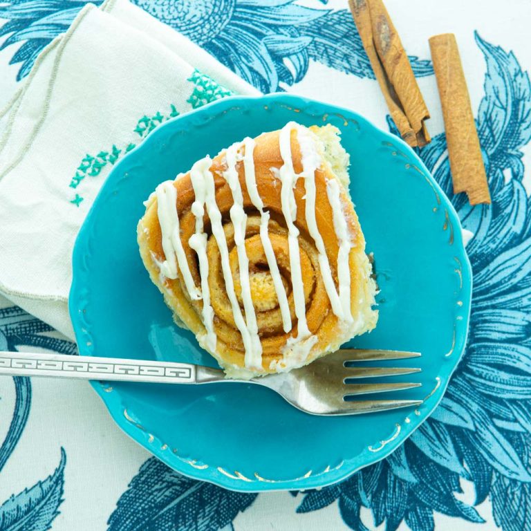 overnight cinnamon roll on plate with fork, napkin and cinnamon sticks
