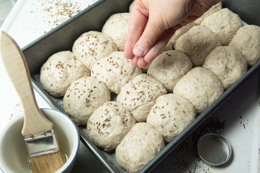 sprinkling caraway on deli rye pan buns