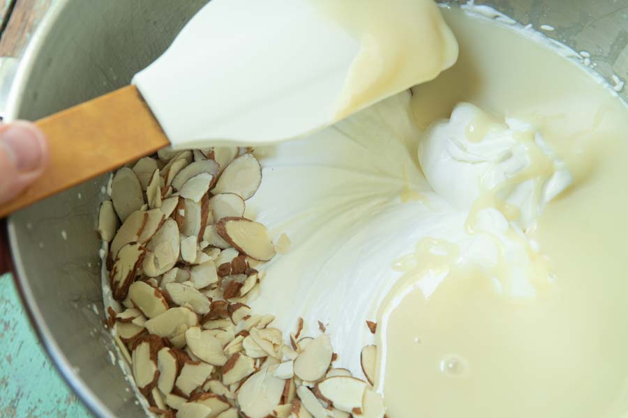 pouring almonds and sweetened condensed milk into cream