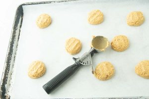 cookie scoop and pumpkin cookie dough balls, flattened on cookie sheet