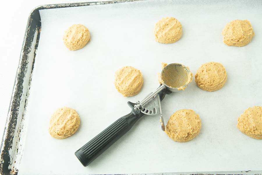 cookie scoop and pumpkin cookie dough balls, flattened on cookie sheet