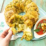 pulling off a piece of pesto monkey bread on plate with marinara sauce