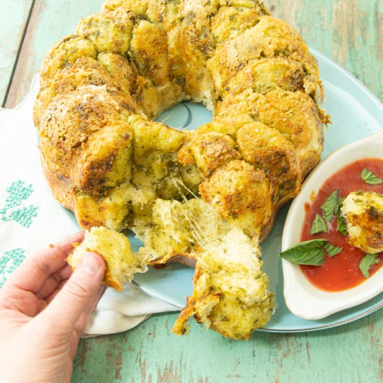 pulling off a piece of pesto monkey bread on plate with marinara sauce