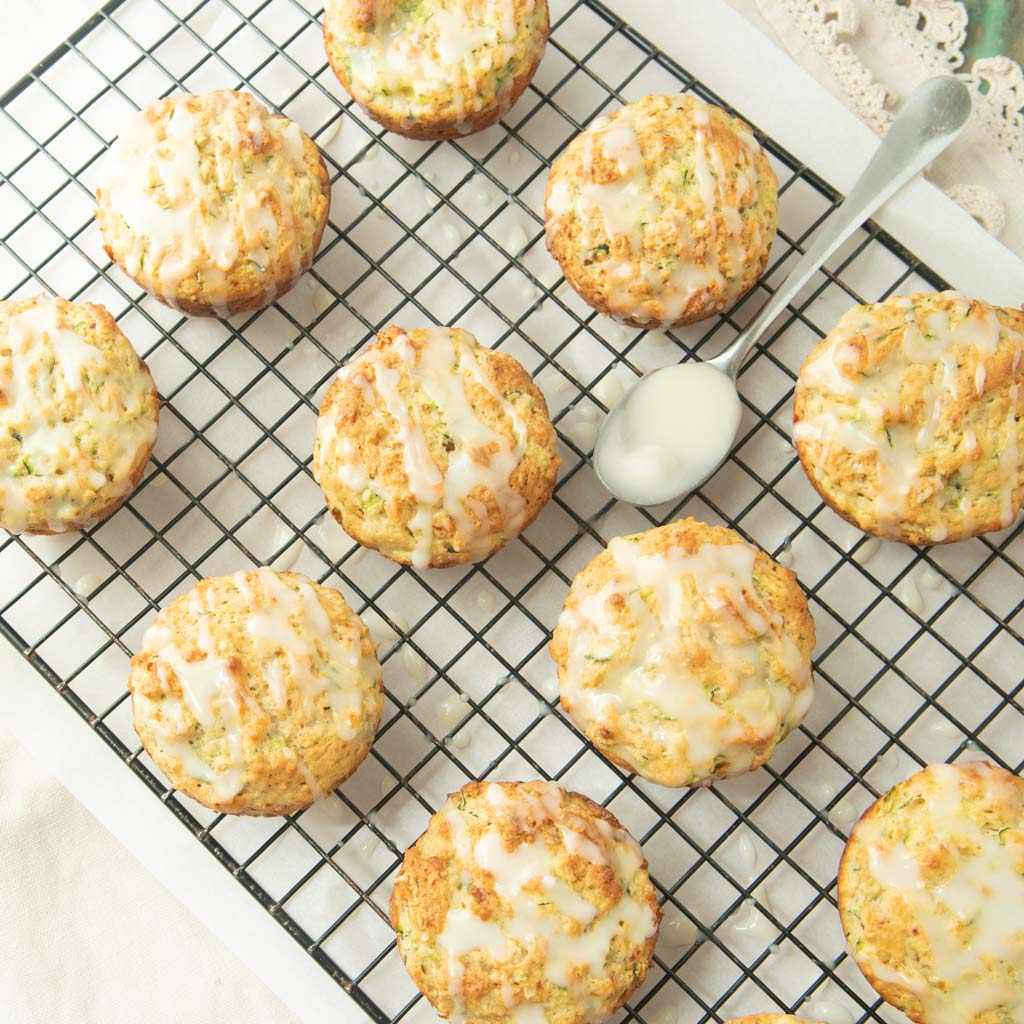 lemon zucchini muffins on wire rack with spoon filled with lemon glaze