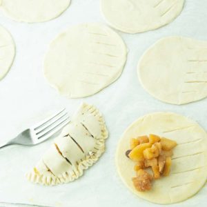 crimping edges of pie dough crust over apple filling on mini apple hand pies