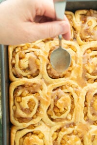 spooning apple butter glaze over apple pie rolls