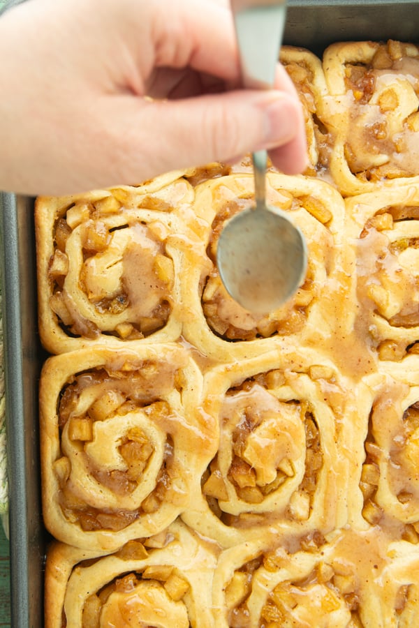 spooning apple butter glaze over apple pie rolls