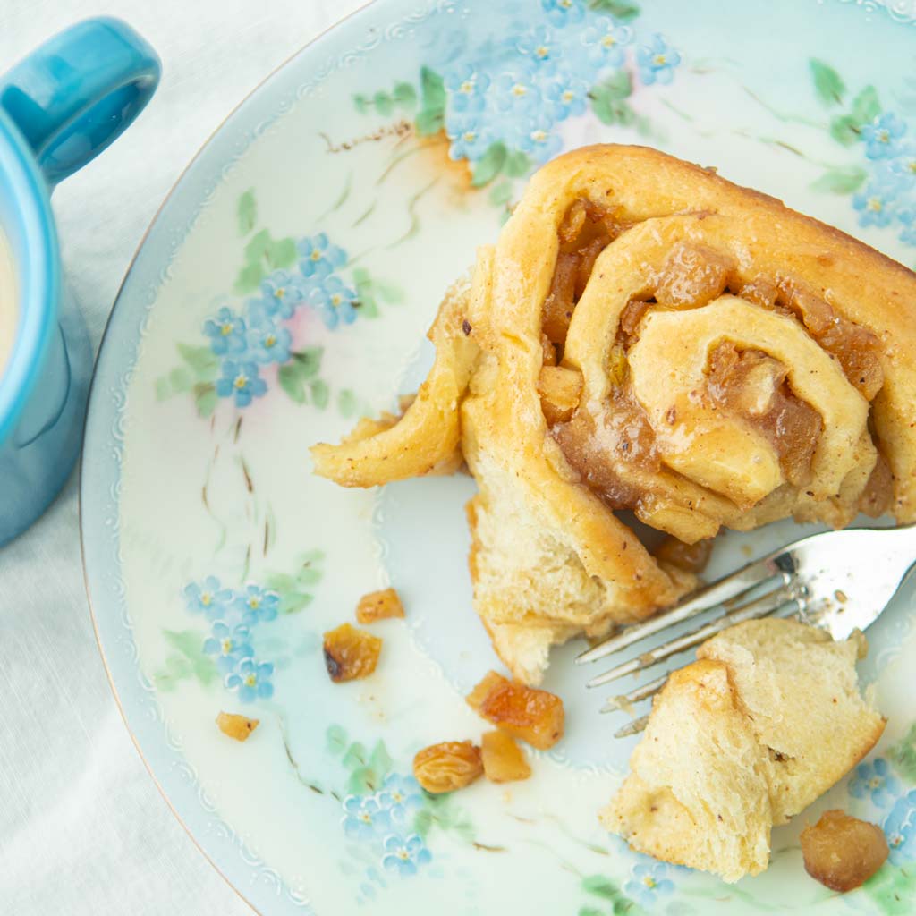 closeup of cinnamon apple pie roll on plate with fork and coffee