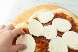 placing slices of mozzarella over tomato sauce on pizza crust