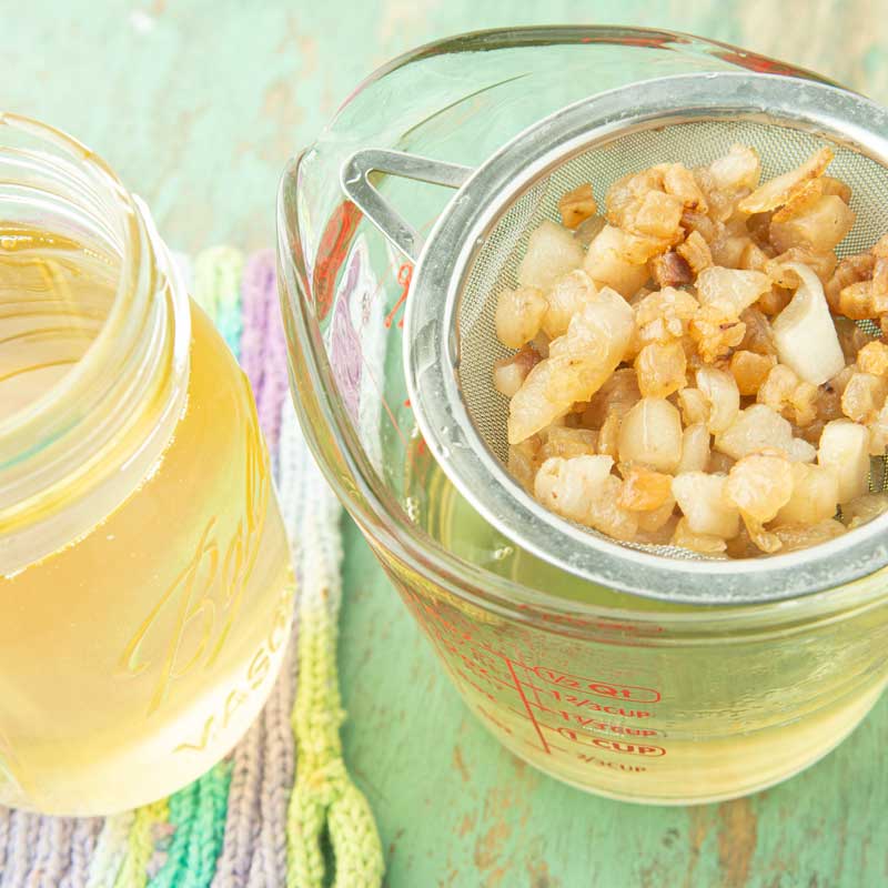 straining lard into glass measuring cup with jar of Mason jar of lard