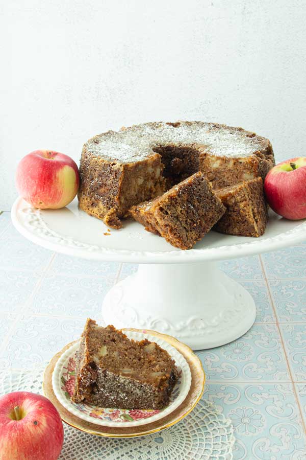 apple cake on cake stand with whole apples and slices of apple cake