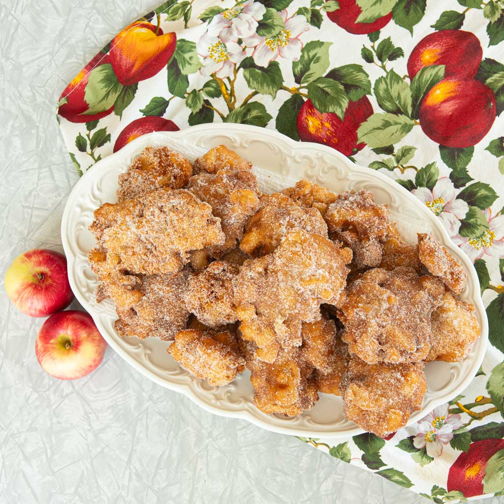 platter of apple fritters with whole apples on apple tablecloth