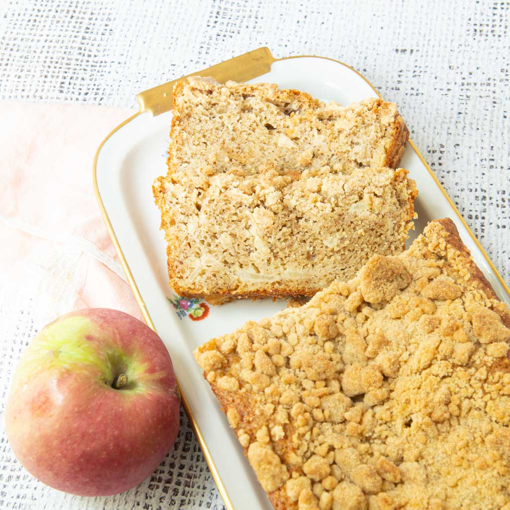 sliced applesauce bread with crumb topping on plate with whole apple