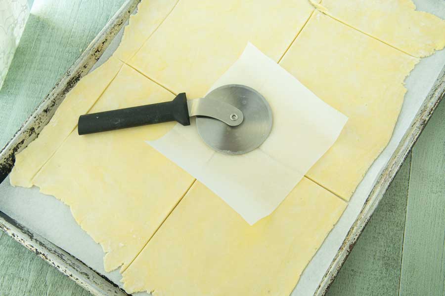 cutting dough around paper template with pizza wheel