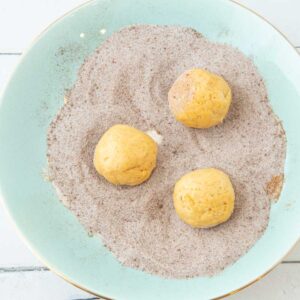 rolling pumpkin snickerdoodle dough in sugar