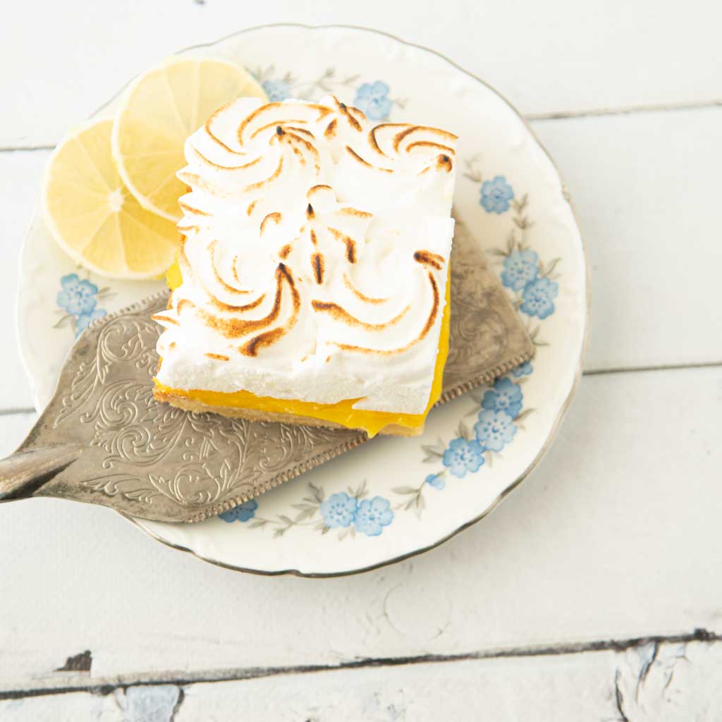 lemon meringue bar on plate with pie server and lemon slices