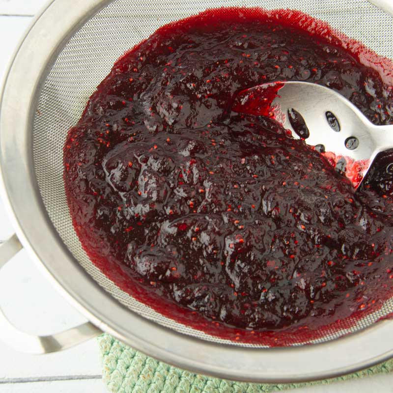 pressing cranberries through fine mesh strainer with spoon
