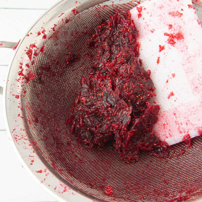 pressing cranberry pulp through strainer with dough scraper