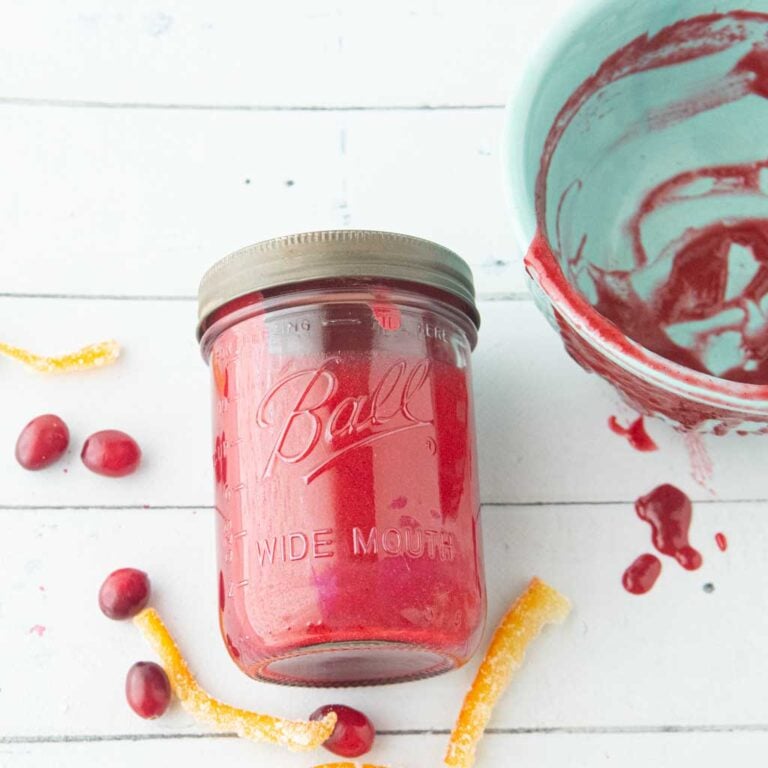 cranberry curd in jar next to bowl, candied orange peel and whole cranberries
