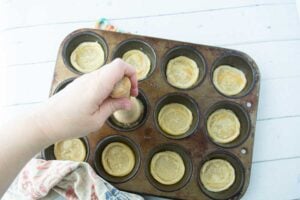 using a tart tamper to squash down puff pastry into muffin tin