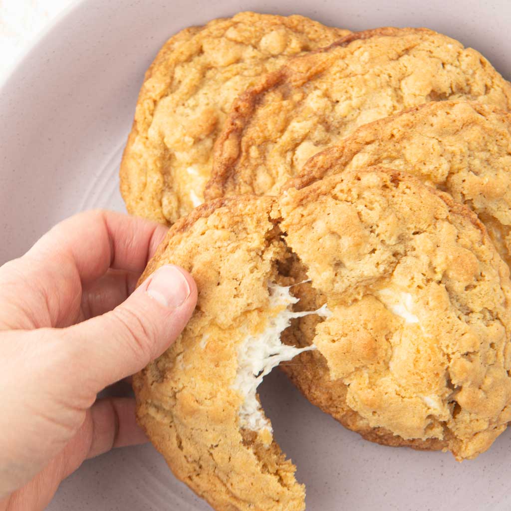 pulling apart a marshmallow crispy cookie in a bowl of cookies