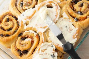 spreading cream cheese frosting on rolls