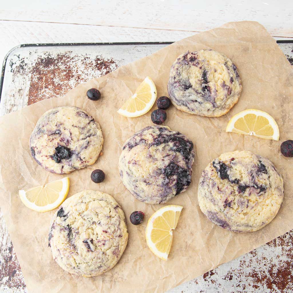 lemon blueberry cookies on cookie sheet next to lemon slices and blueberries