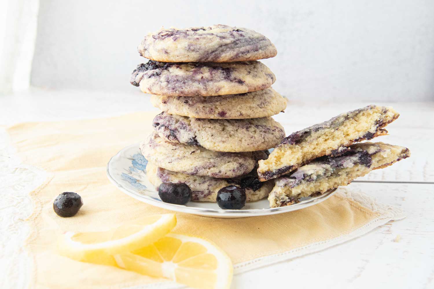 stack of lemon blueberry cookies next to lemon slices and blueberries