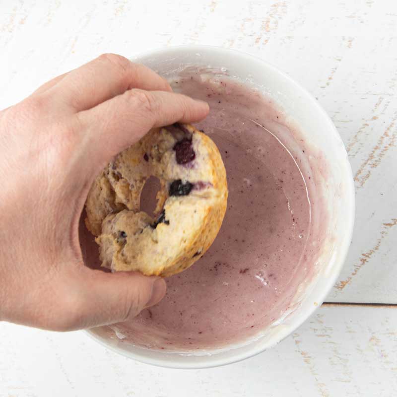 dipping lemon blueberry donut into blueberry glaze