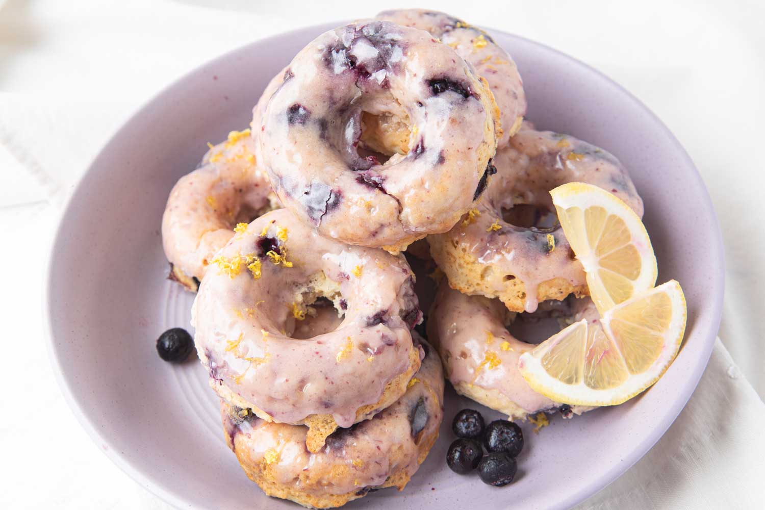 bowl of a stack of lemon blueberry donuts with lemon slices and whole blueberries.