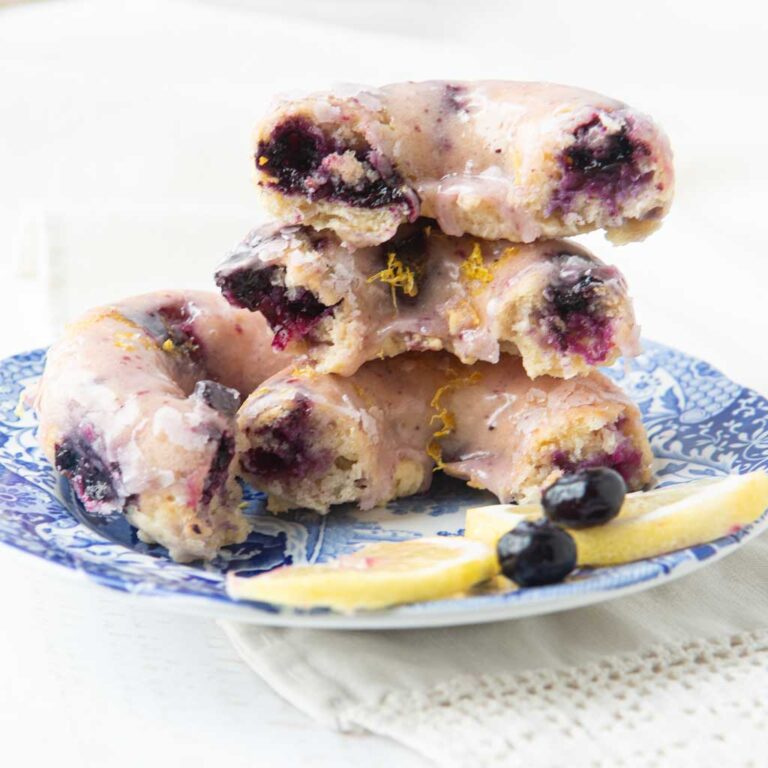 stack of cross section pieces of lemon blueberry donuts on plate with lemon slices and whole blueberries