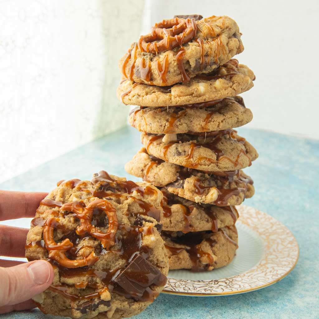 hand holding pretzel cookie next to stack of caramel chocolate chip pretzel cookies