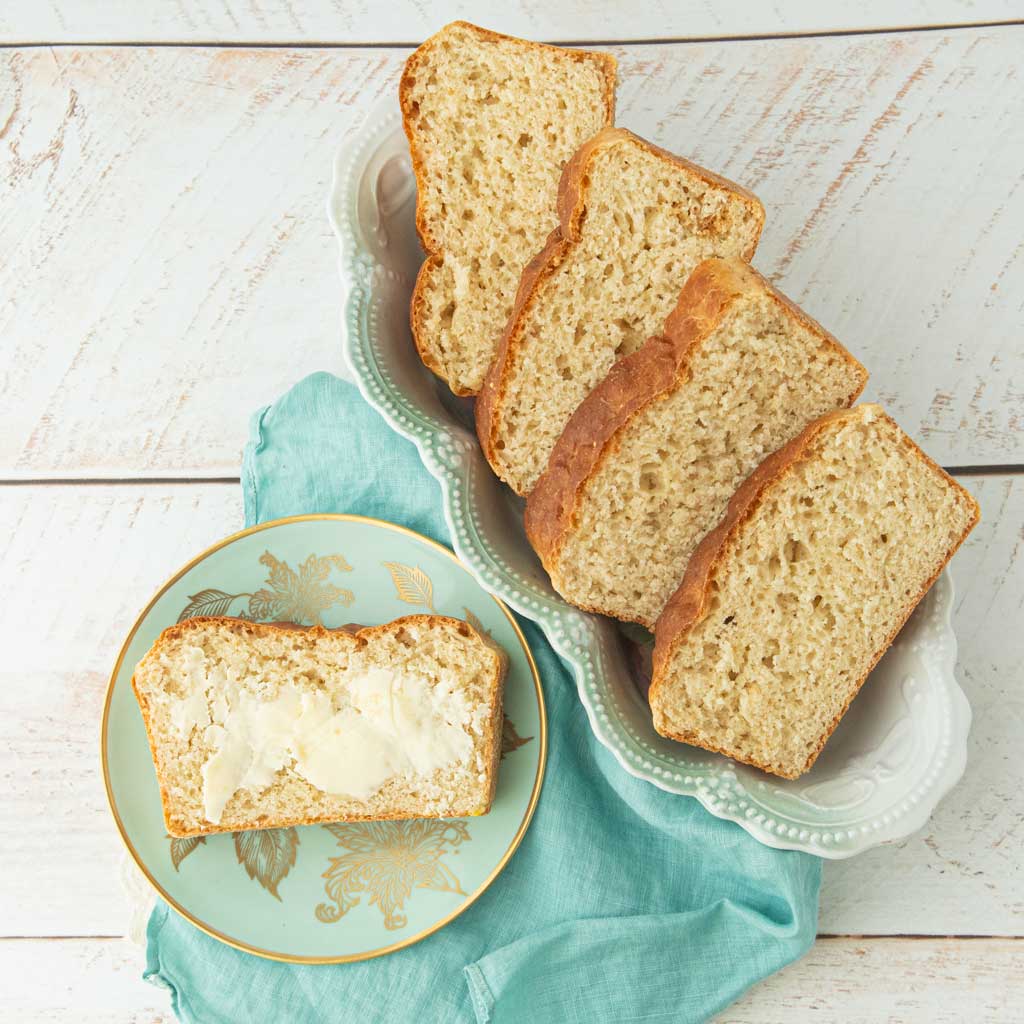 slice of English muffin bread with butter on it next to platter with slices of English muffin bread