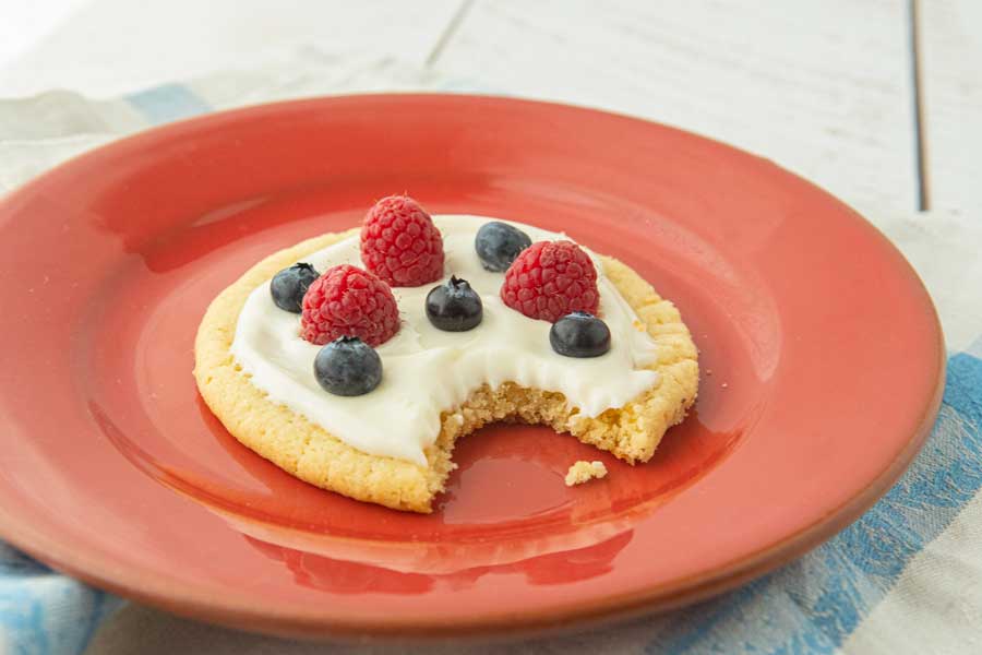 side view of fruit pizza cookie on red plate with bite taken out of it