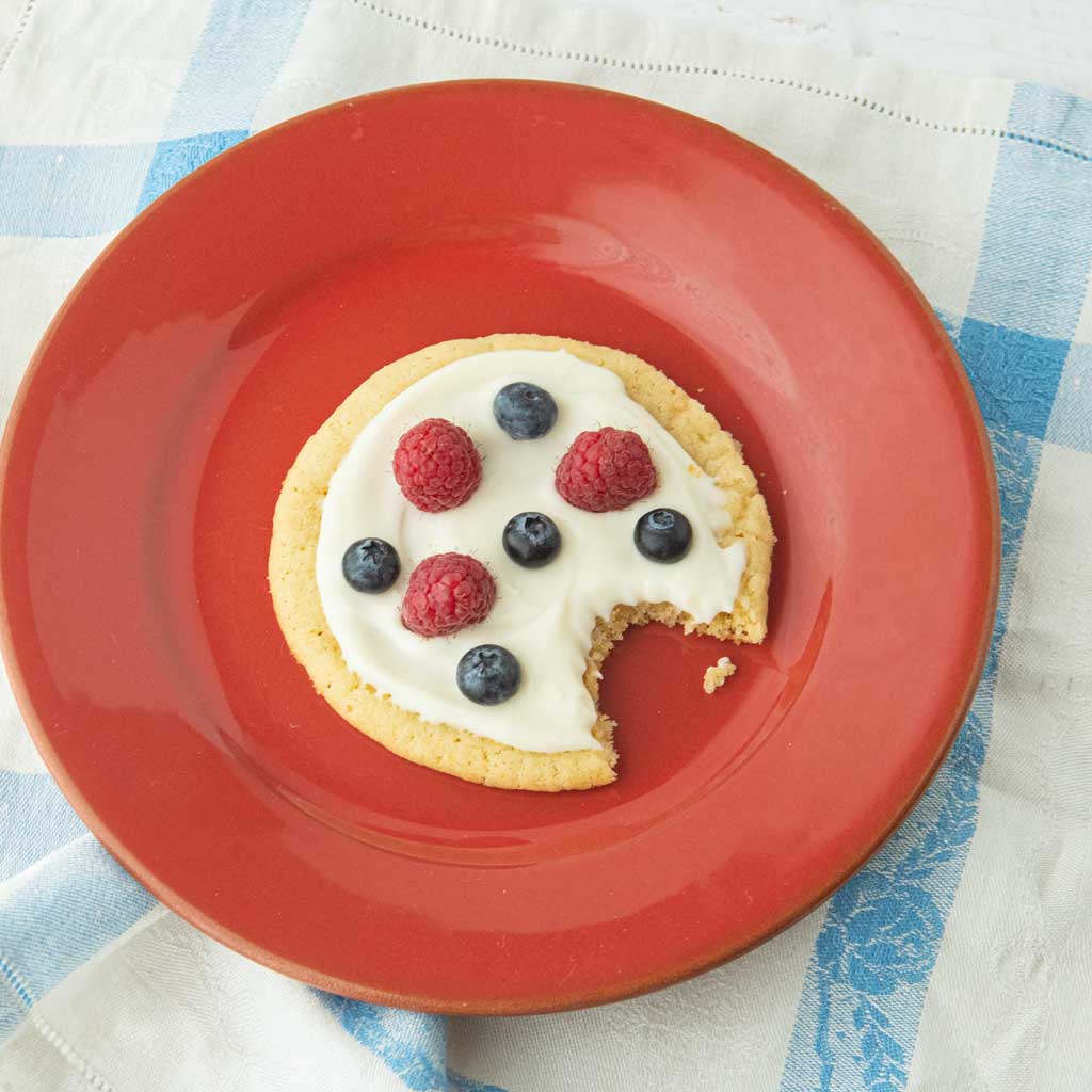 top view of fruit pizza cookie on red plate with bite taken out of it