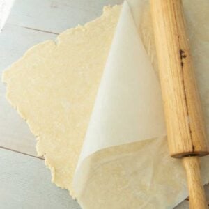 rolling cream cheese pastry dough between sheets of parchment, rolling pin