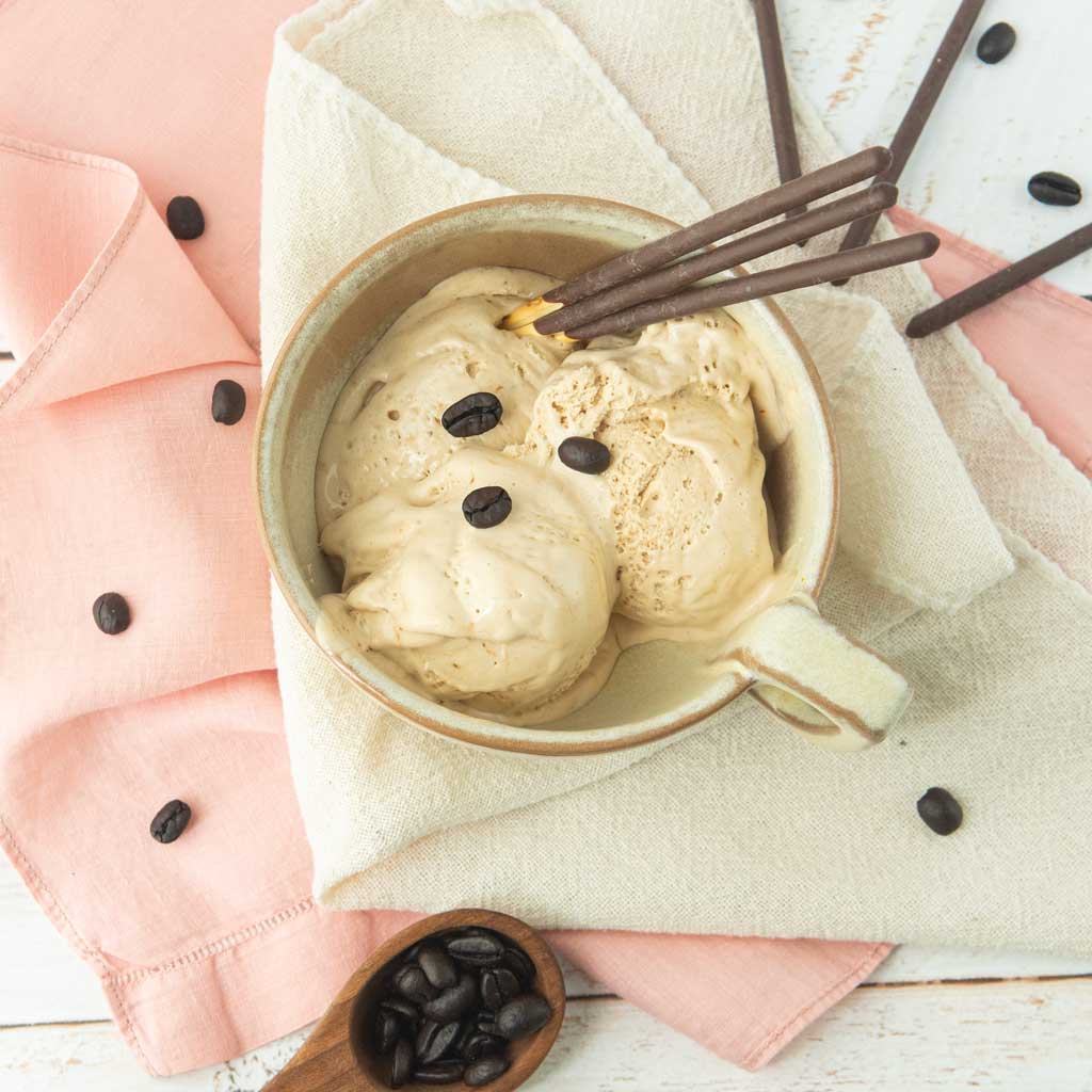coffee ice cream in beige cup with chocolate Pocky sticks, coffee scoop and coffee beans