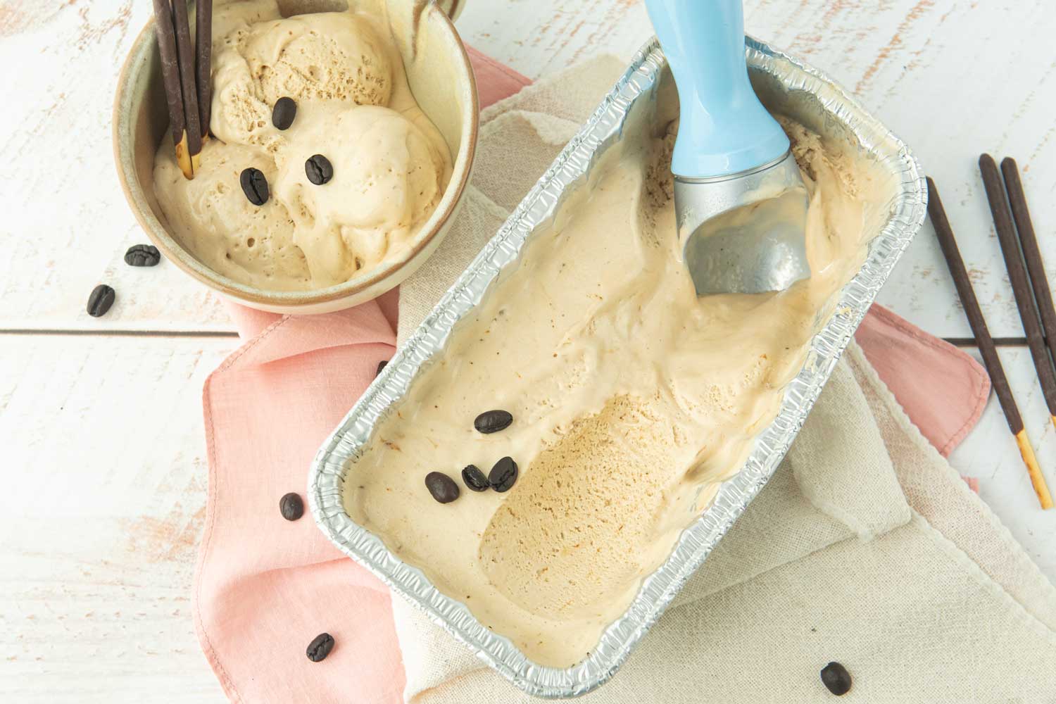 coffee ice cream in beige cup with chocolate Pocky sticks, ice cream scoop in loaf pan of coffee ice cream