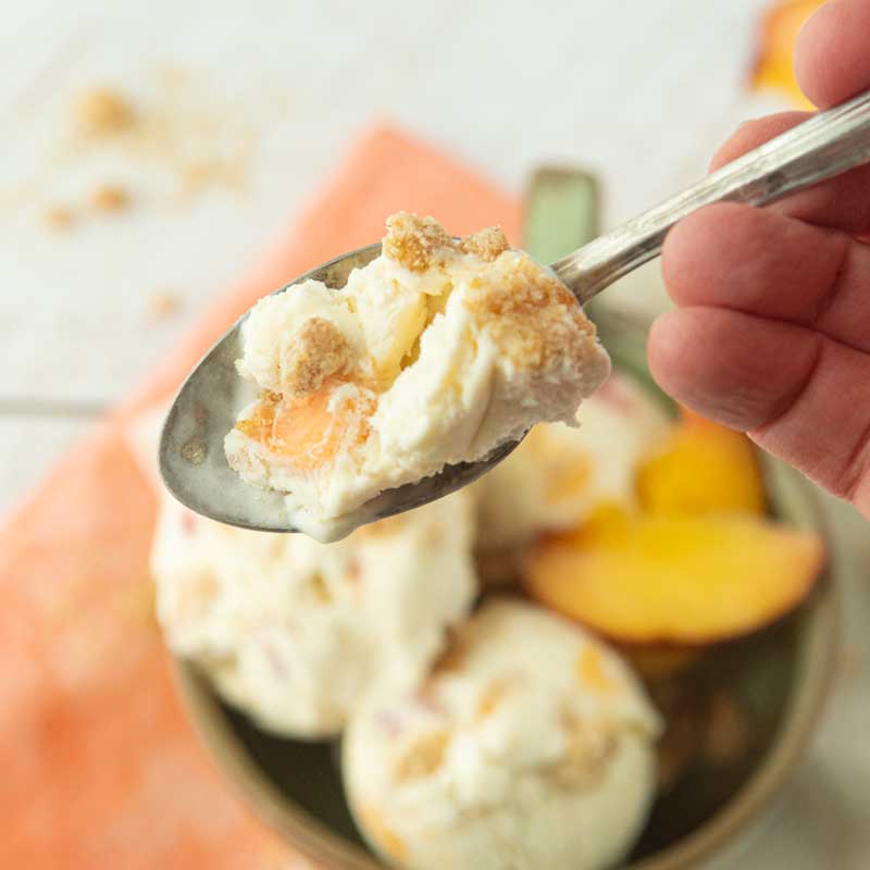 hand showing closeup of spoon of peach ice cream