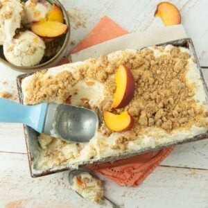 peach ice cream in loaf pan with ice cream scoop next to slices of peaches and dish of peach crumble ice cream