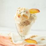 peach ice cream in glass dish with peach slices on op of white and peach napkins