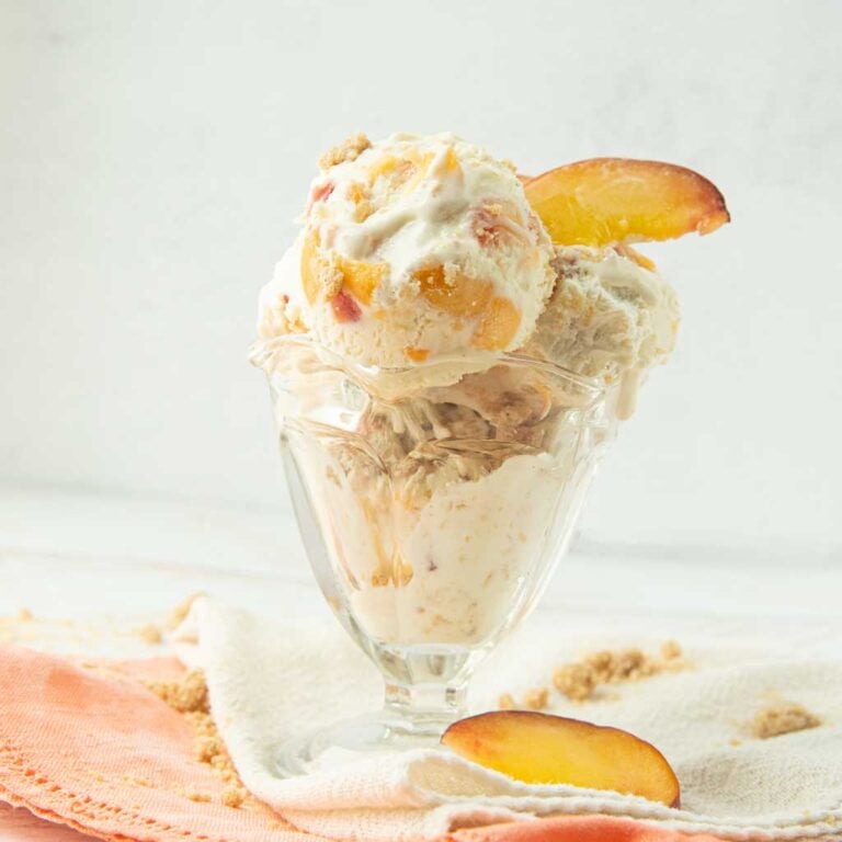 peach ice cream in glass dish with peach slices on op of white and peach napkins