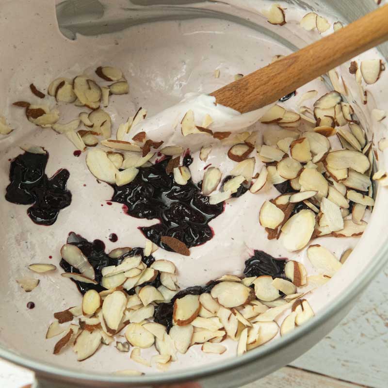 folding almonds and cooked cherries into whipped cream for cherry ice cream